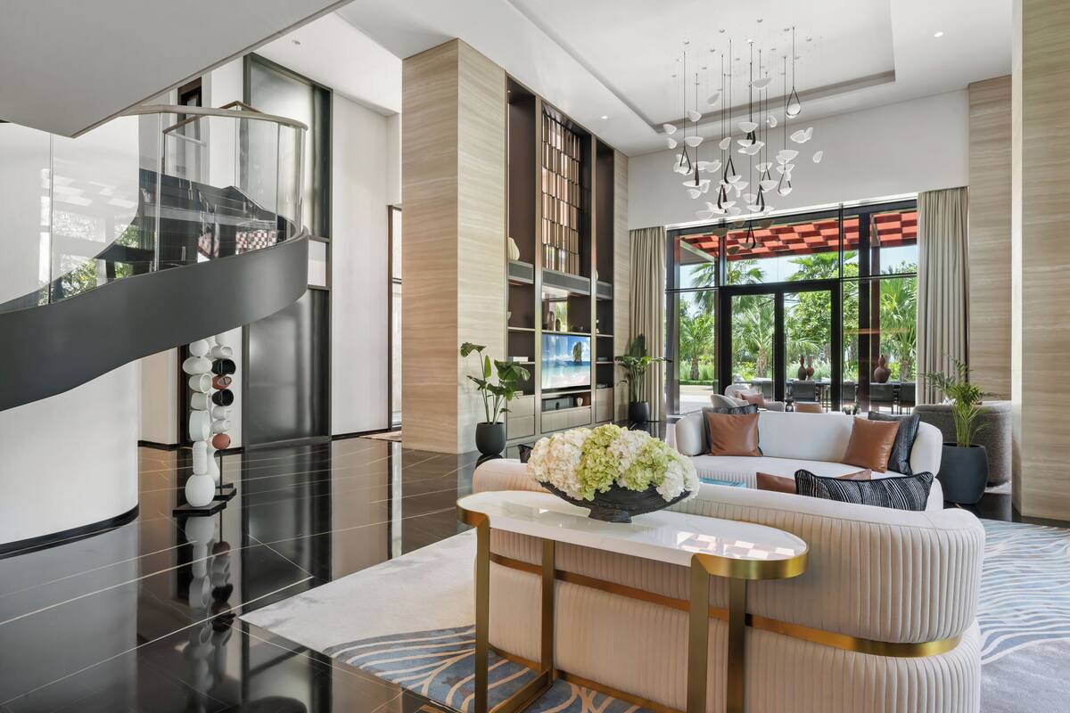 A modern living room with a curved sofa, a glass staircase, and a large window with a view of greenery.