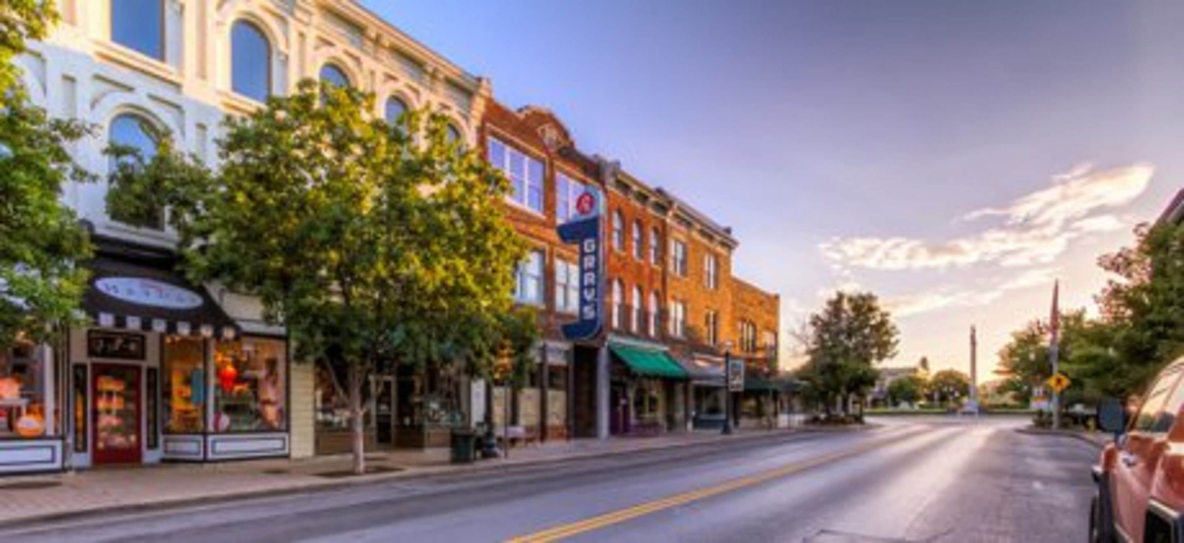 A street view with historic buildings, storefronts, and a clear sky.