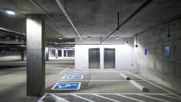 A parking garage with concrete pillars, marked parking spaces, and a visible elevator.