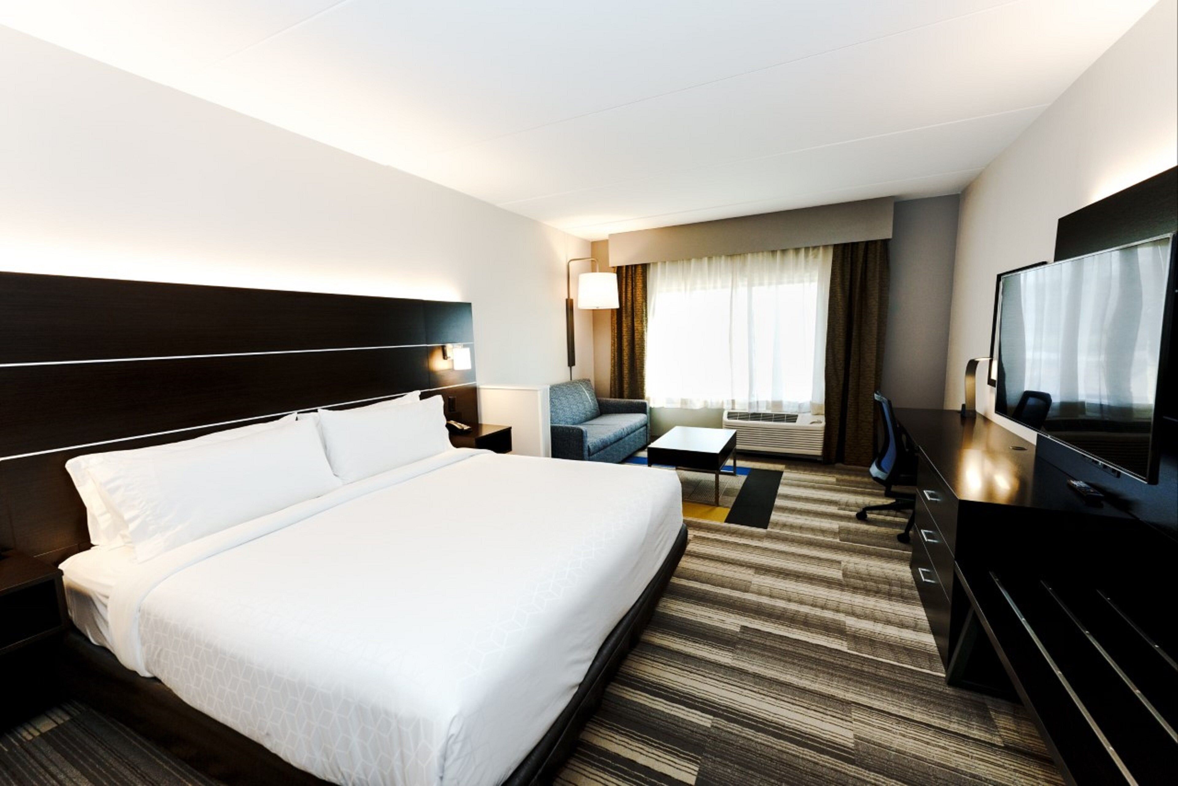 Une chambre d’hôtel dotée d’un grand lit, d’un bureau, d’une télévision et d’un coin salon avec un canapé et un fauteuil.