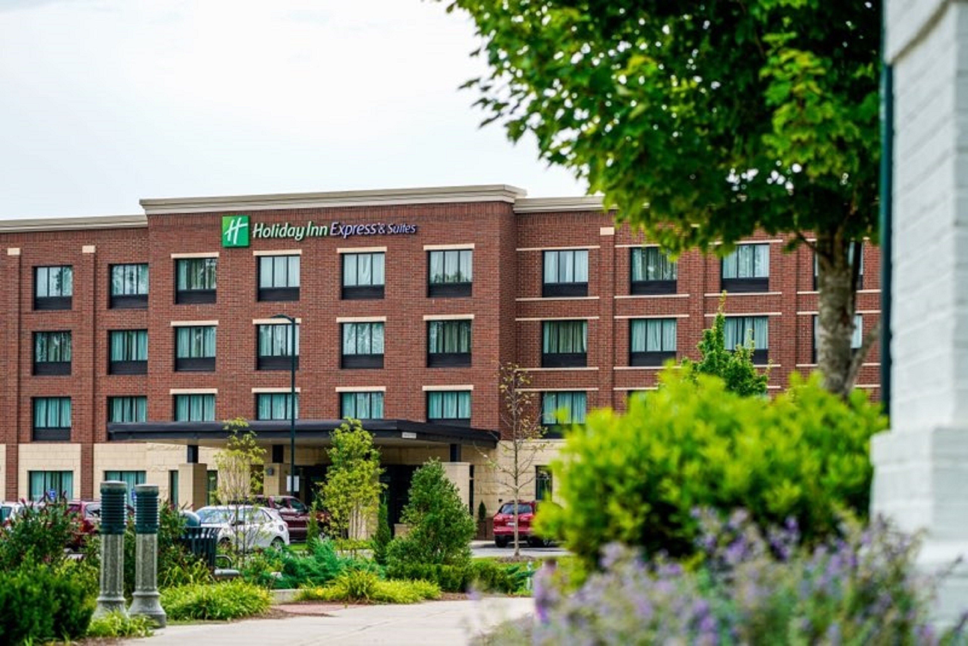 Edificio de Holiday Inn Express & Suites con fachada de ladrillo, varias ventanas y un estacionamiento con coches.