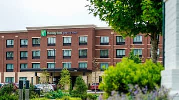 A Holiday Inn Express & Suites building with a brick facade, multiple windows, and a parking lot with cars.