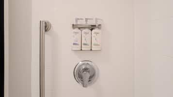A bathroom with a white tiled wall, a chrome showerhead, and three Dove products on a shelf.