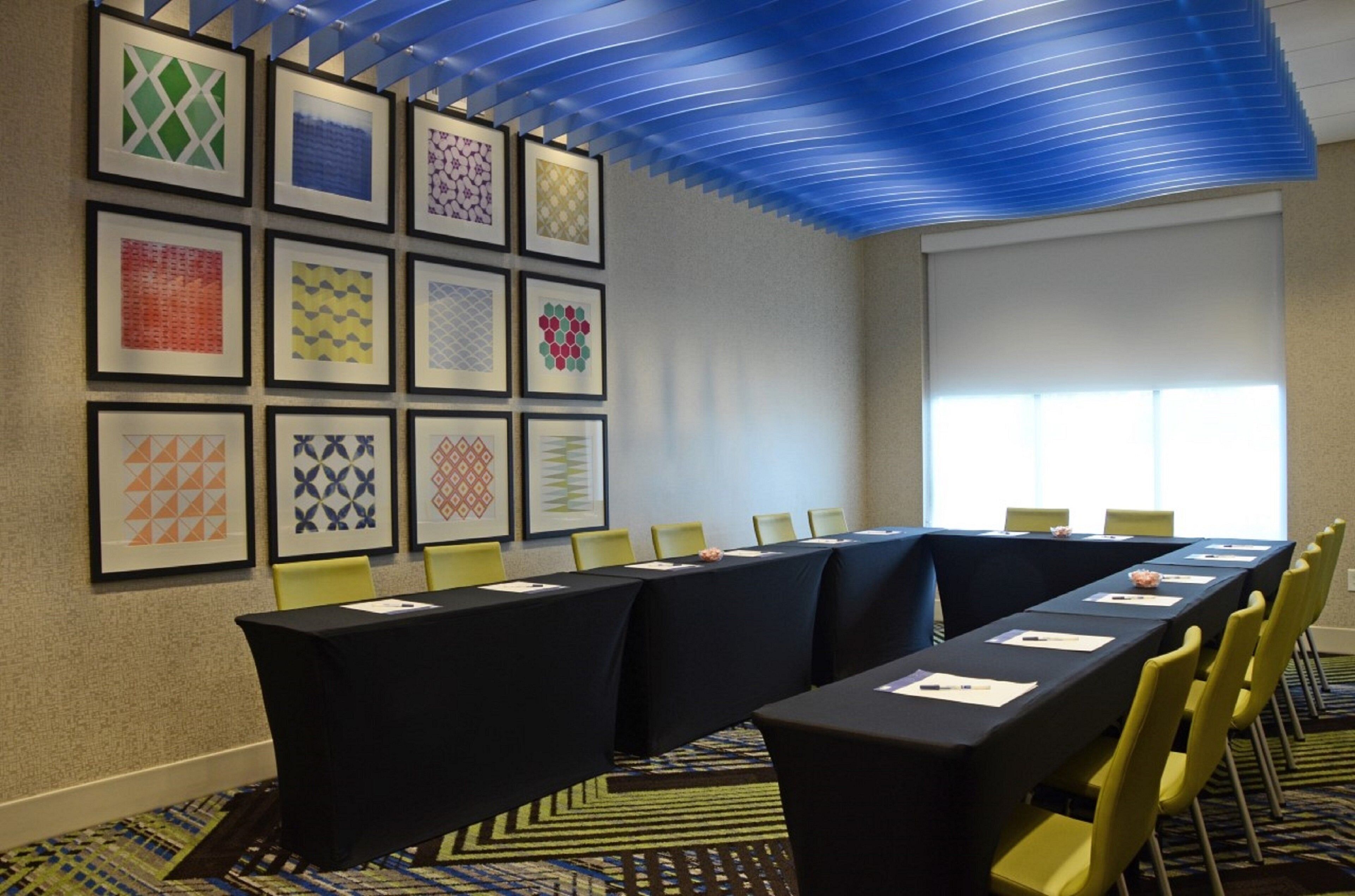 A conference room with a long table, yellow chairs, and framed artwork on the wall.