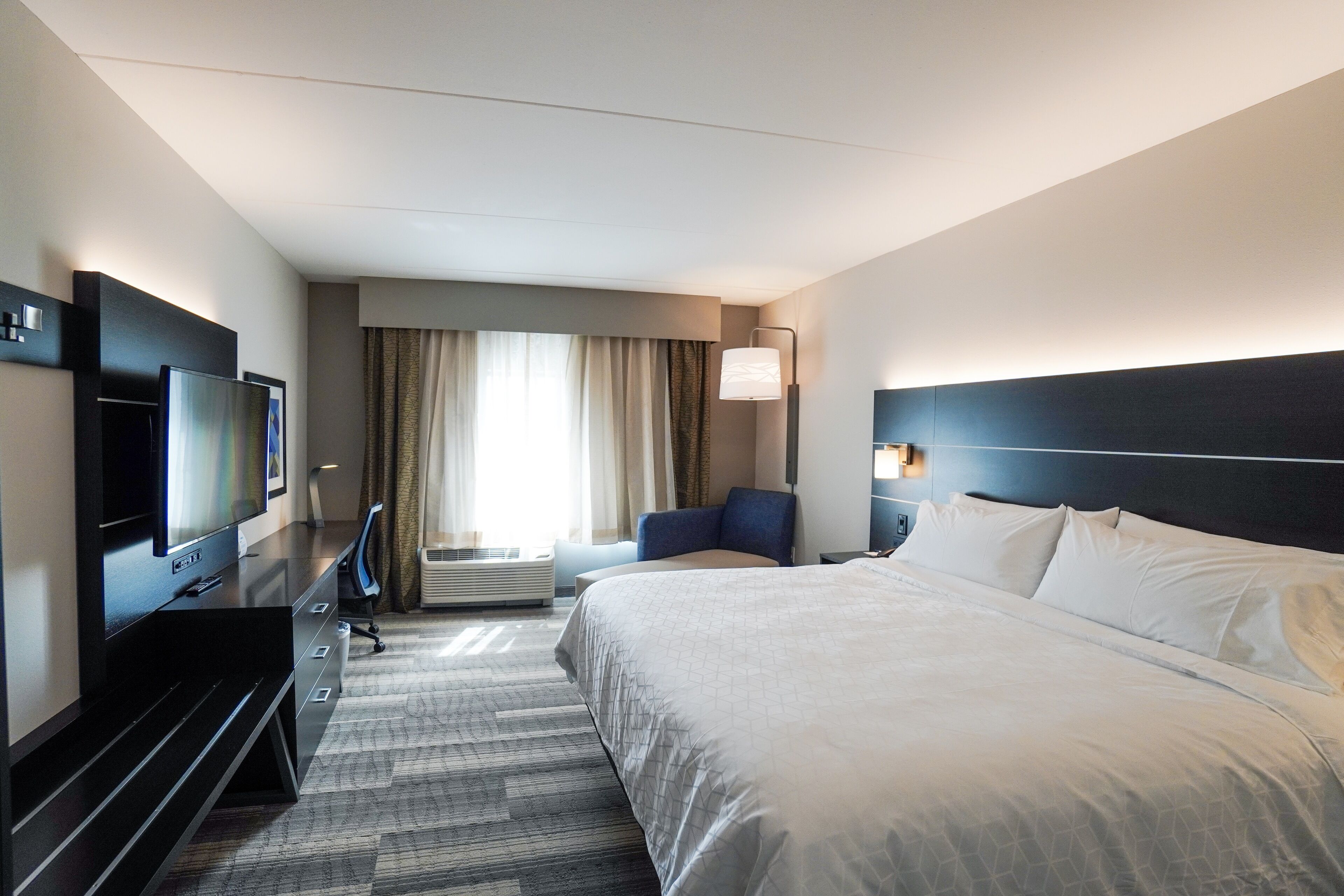 Habitación de hotel con una cama grande, televisión de pantalla plana, escritorio con silla y ventana con cortinas.