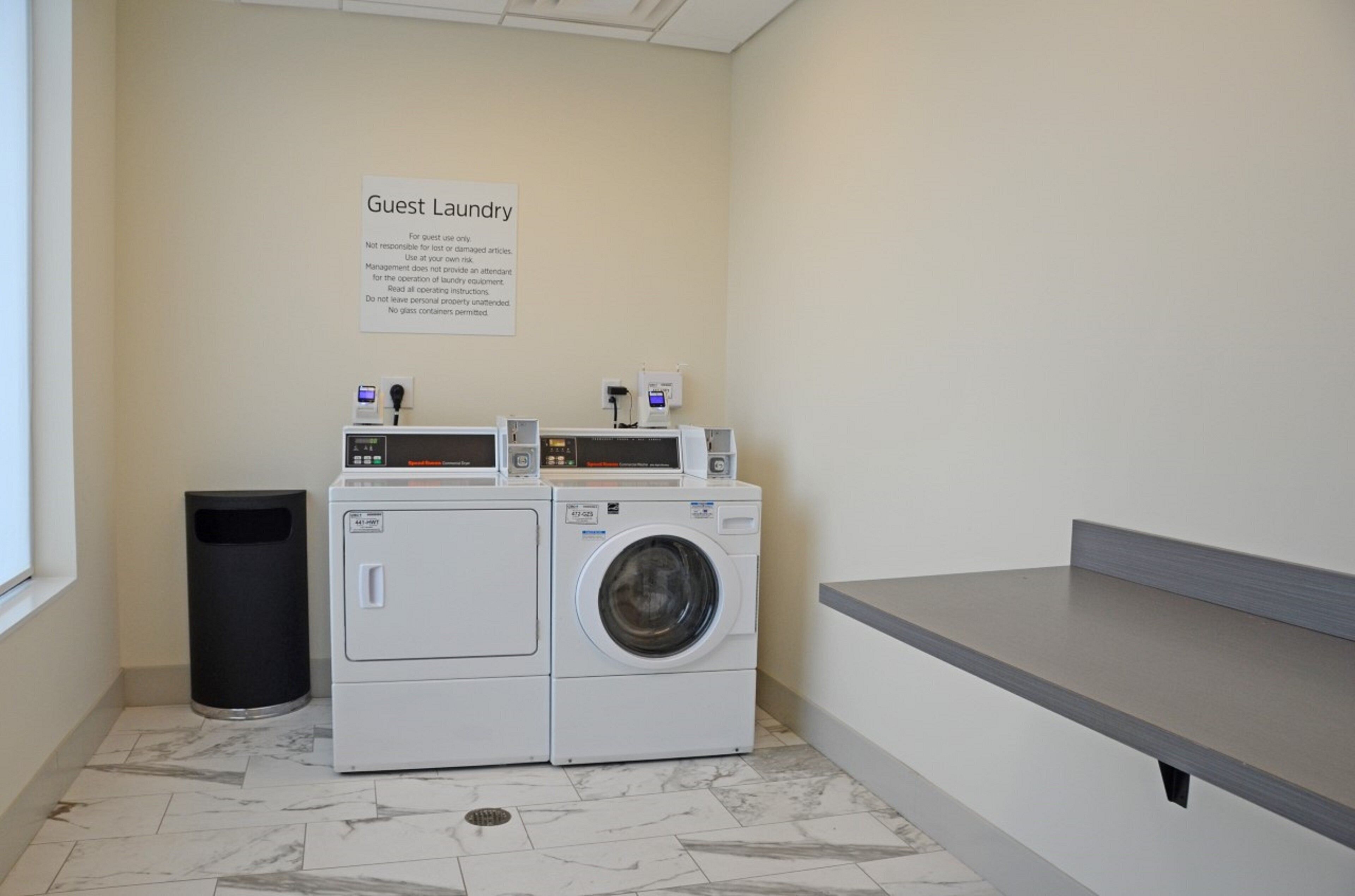 A guest laundry area with a sign indicating it's for guest use only, a washing machine, a dryer, and a trash bin.