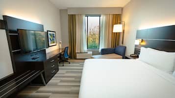 Una habitación de hotel con cama, escritorio, silla, televisor y ventana con cortinas.
