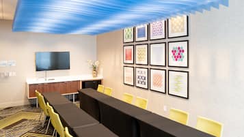 A conference room with a long table, yellow chairs, a flat-screen TV, and framed artwork on the wall.