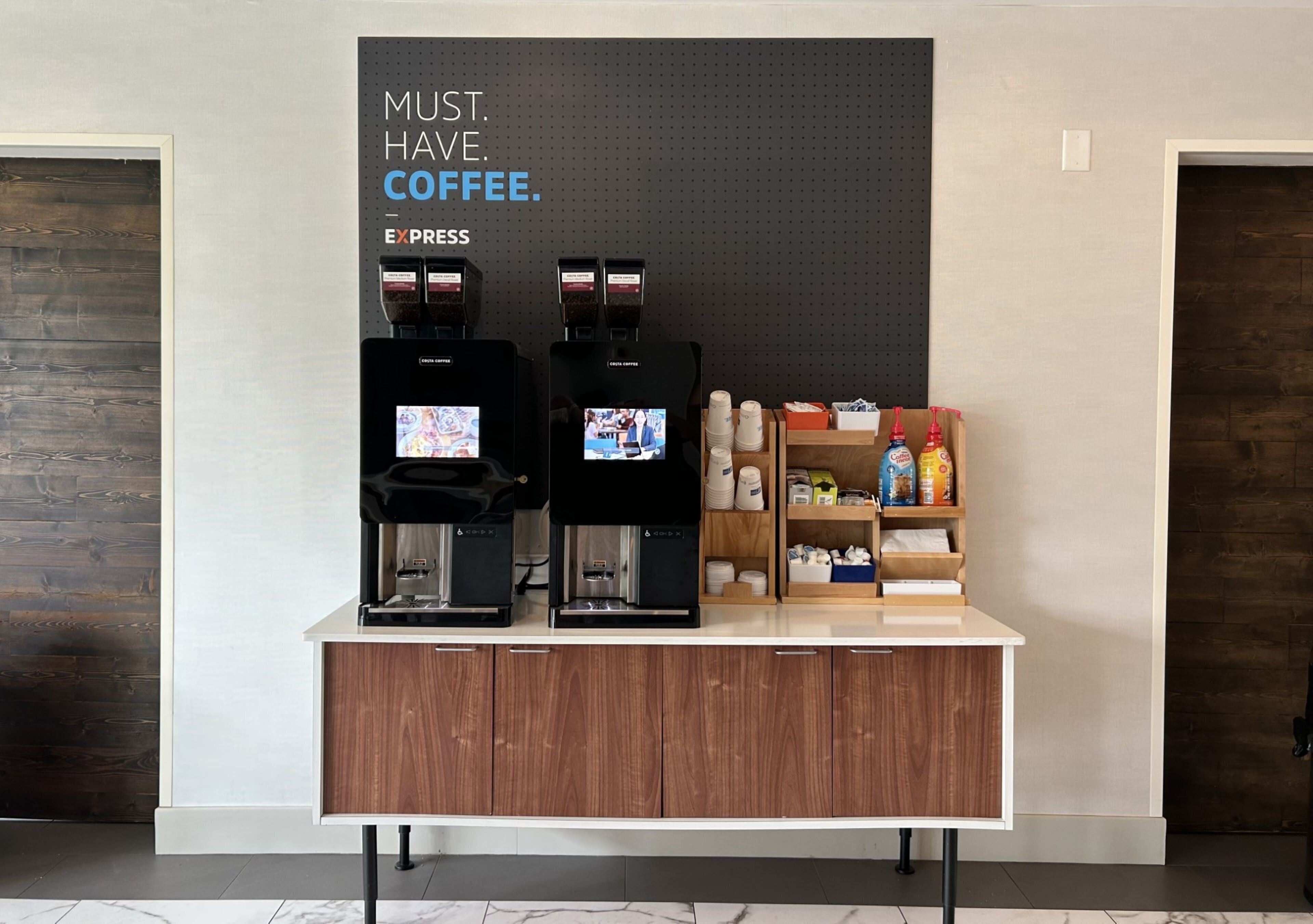 Een koffiehoek met twee espresso machines, een bordje met de tekst 'COFFEE IS VERPLICHT' en een toonbank met diverse koffieartikelen.