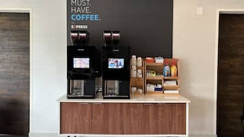 Ein Kaffee-Bereich mit zwei Espressomaschinen, einem Schild mit der Aufschrift 'COFFEE IST EIN MUSS' und einer Theke mit verschiedenen Kaffeeartikeln.