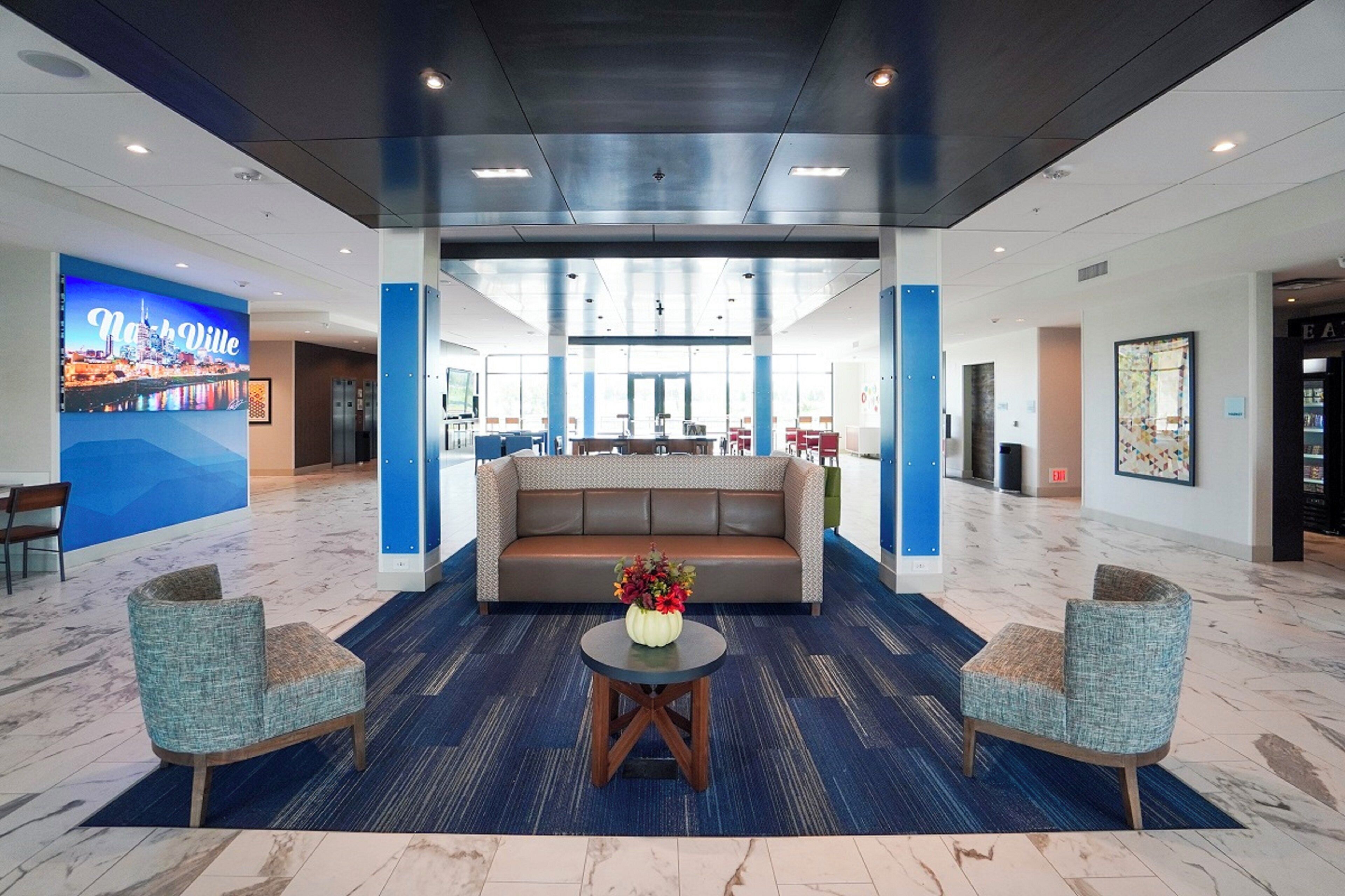 A lobby with a blue carpet, a sofa, two armchairs, and a table with a vase of flowers.