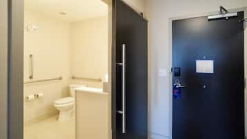 A bathroom with a toilet, handrails, and a towel dispenser.