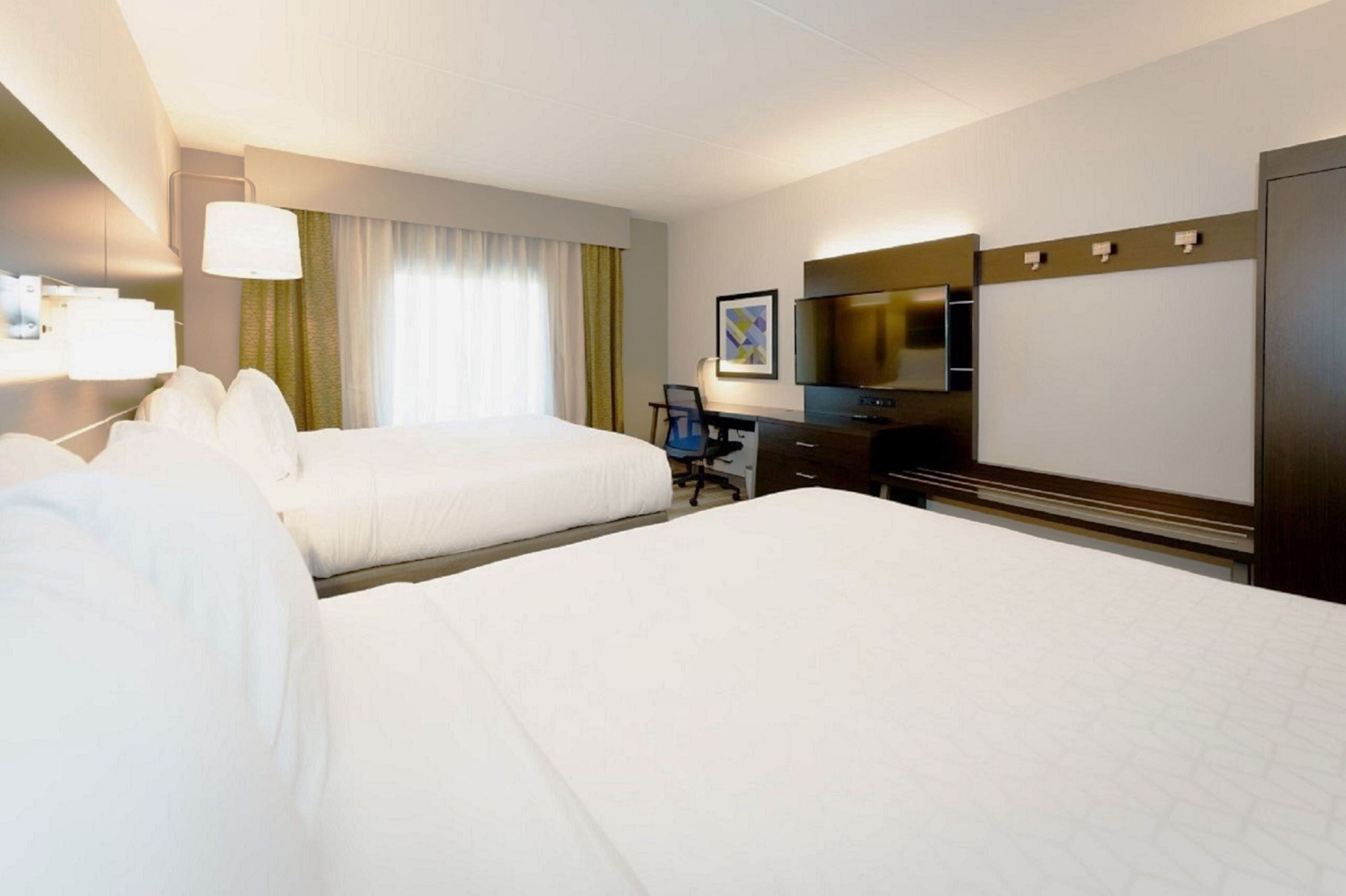 A hotel room with two beds, a desk, a chair, a television, and a large window with curtains.