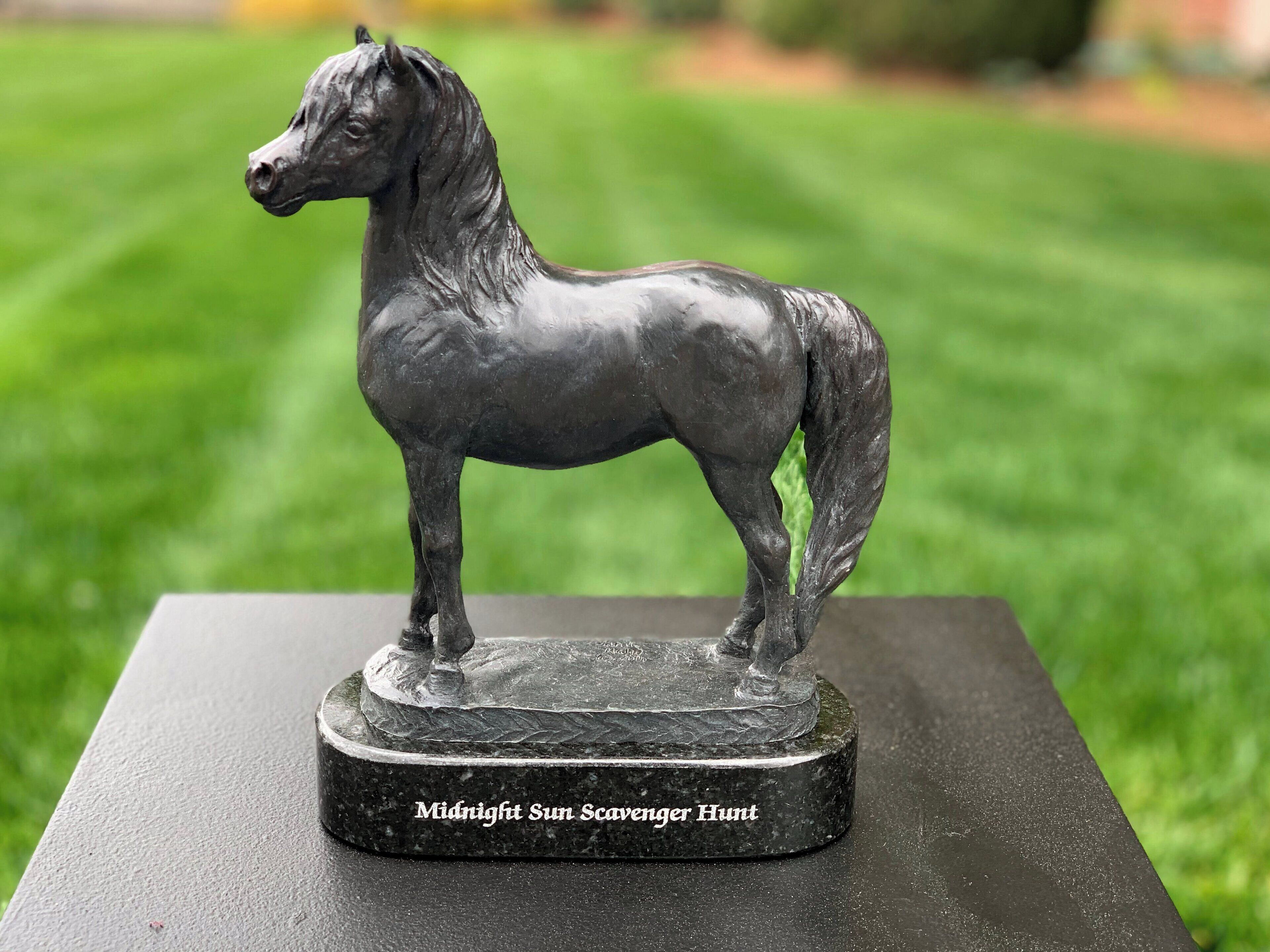 Una estatua de bronce de un caballo sobre un pedestal negro con la inscripción "Midnight Sun Scavenger Hunt".