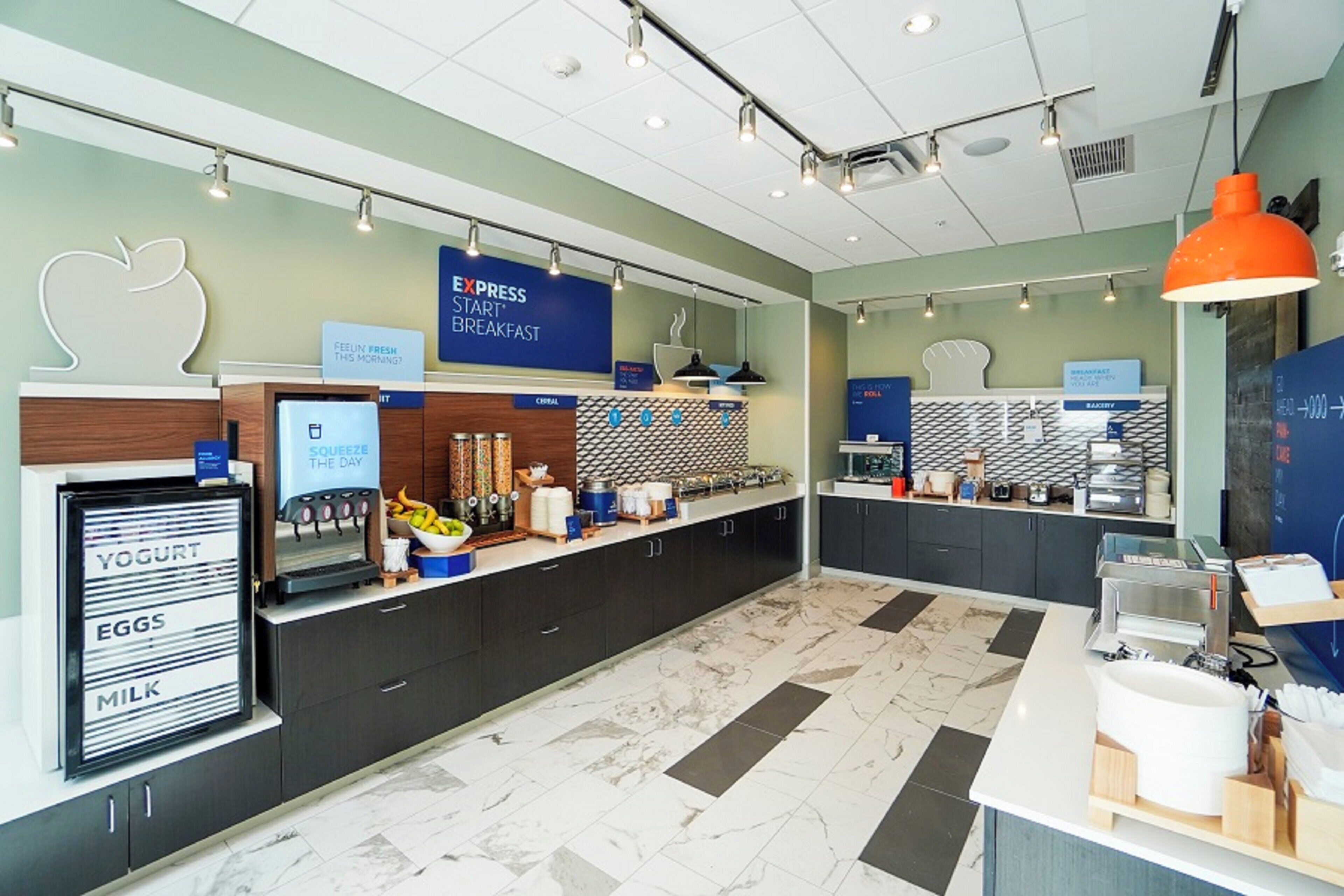 A breakfast area with a yogurt, eggs, and milk dispenser, a blue sign for breakfast, and a counter with various food items.
