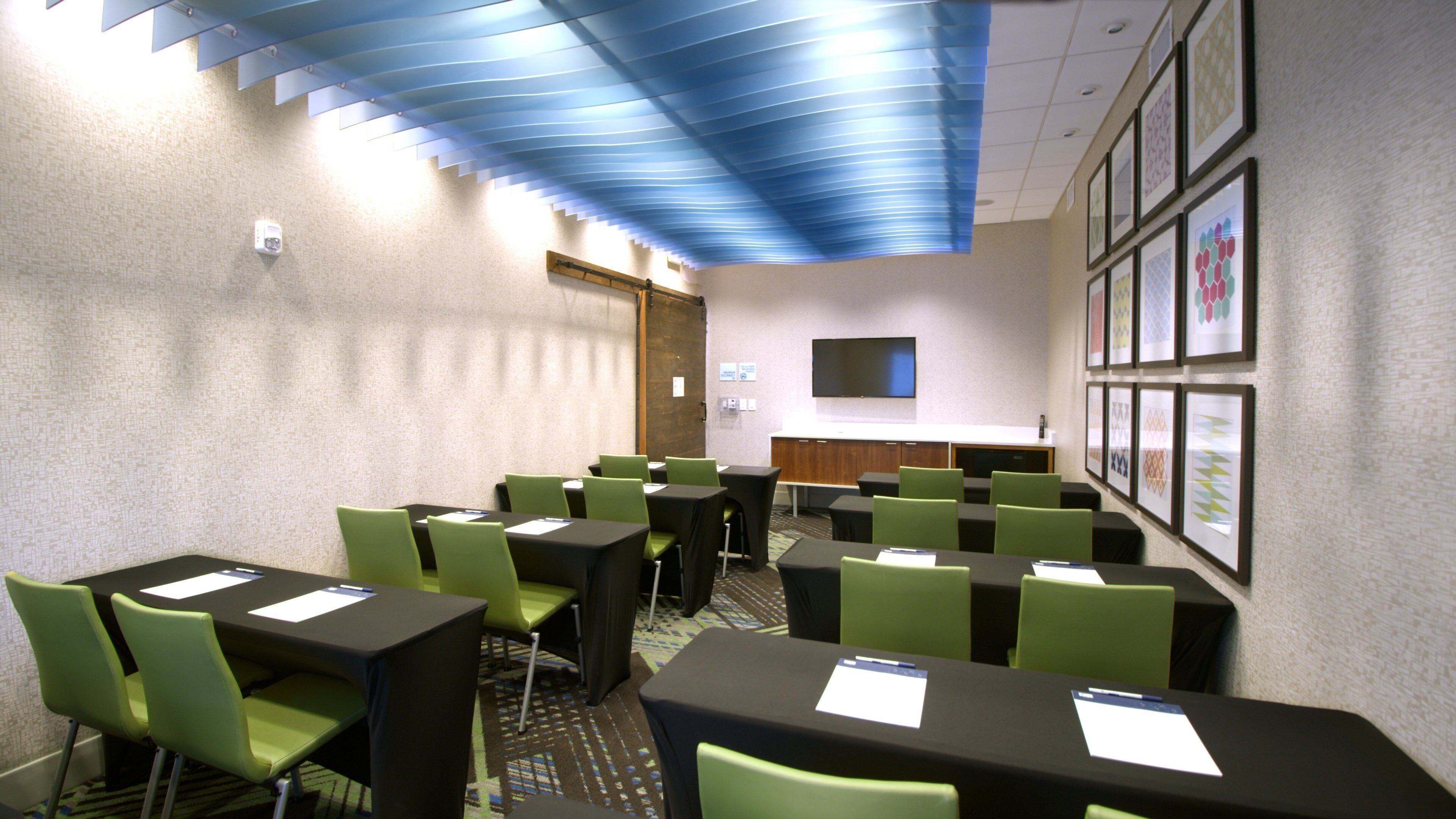 A conference room with tables and chairs, a flat-screen TV, and framed artwork on the walls.
