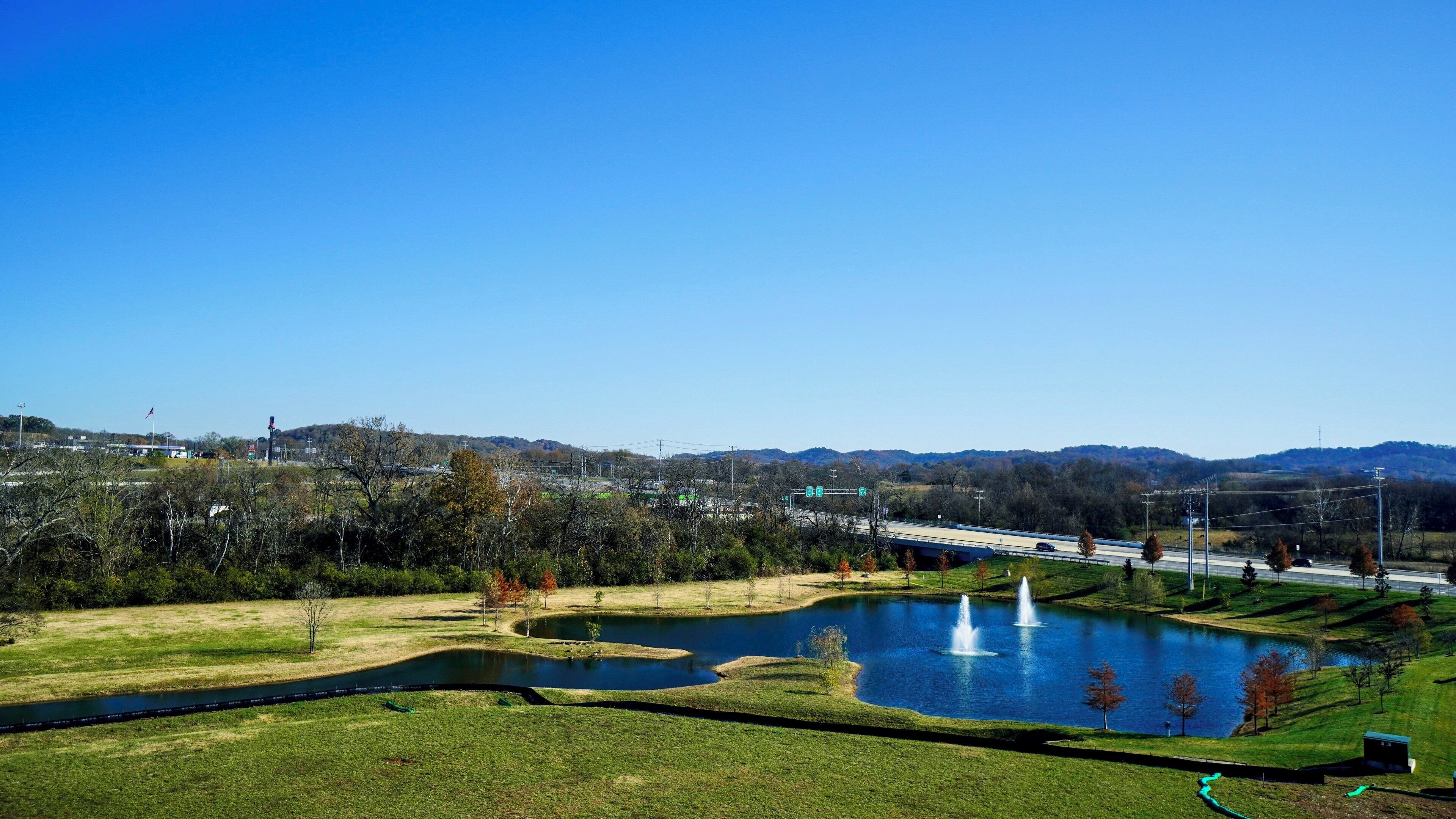 Un parque con un estanque, fuentes y un puente al fondo.