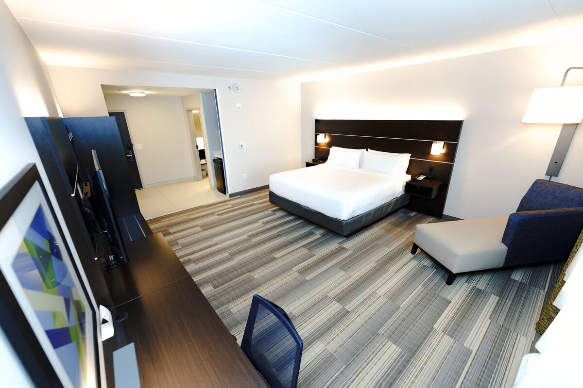 A hotel room with a large bed, a desk with a chair, a TV, and a lamp.