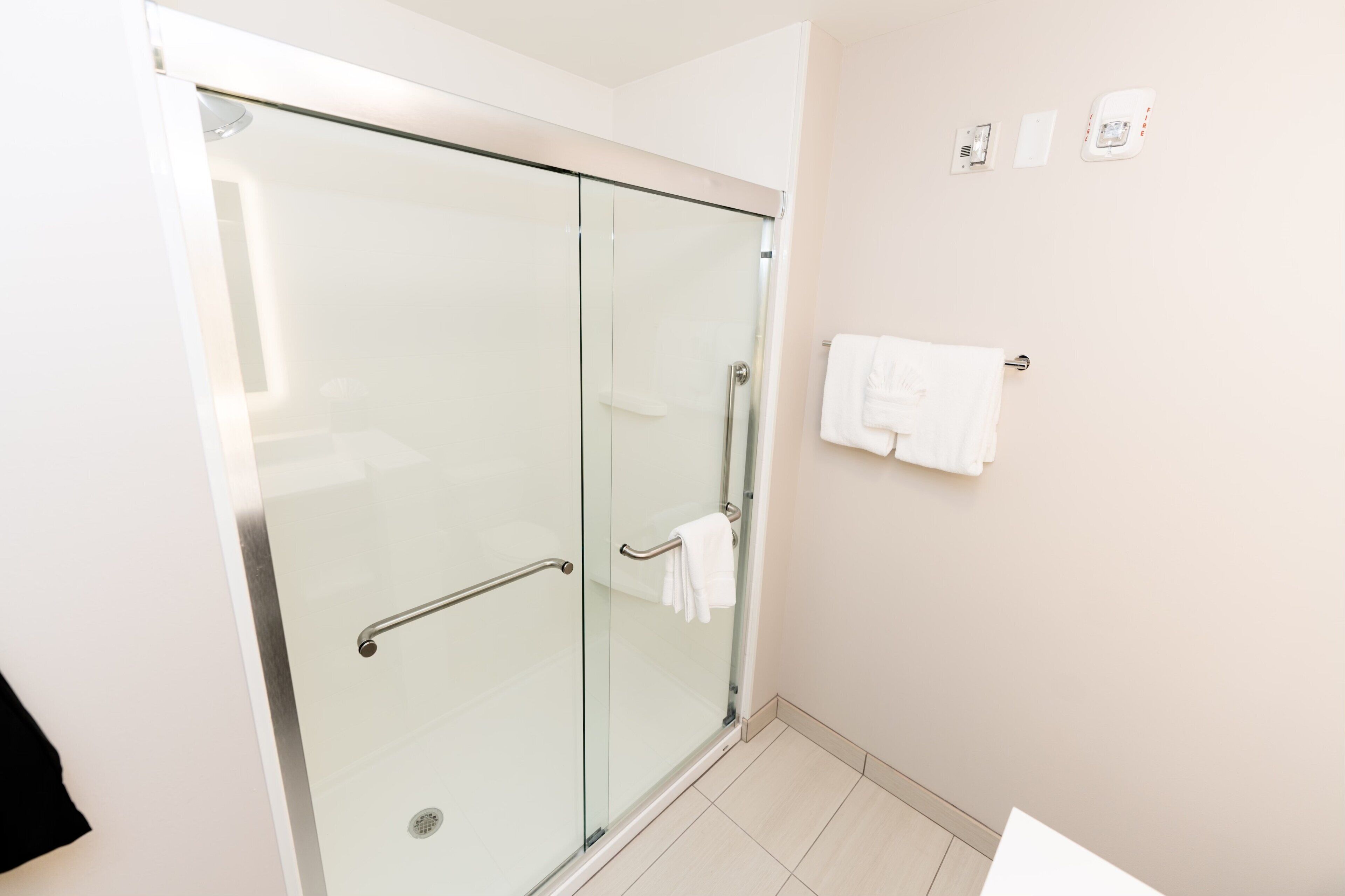 Un baño moderno con ducha de vidrio, un toallero blanco y un dispensador de papel higiénico visible.