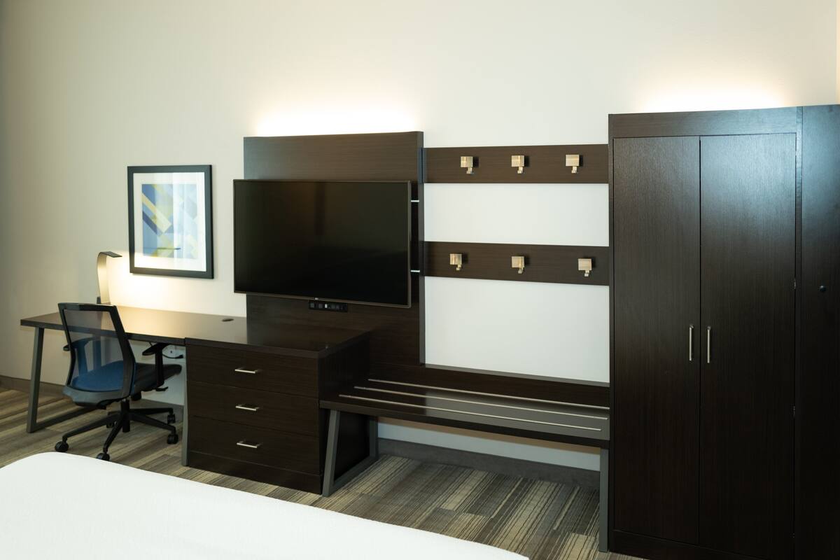 A hotel room with a bed, a desk with a chair, a television, and a wardrobe.