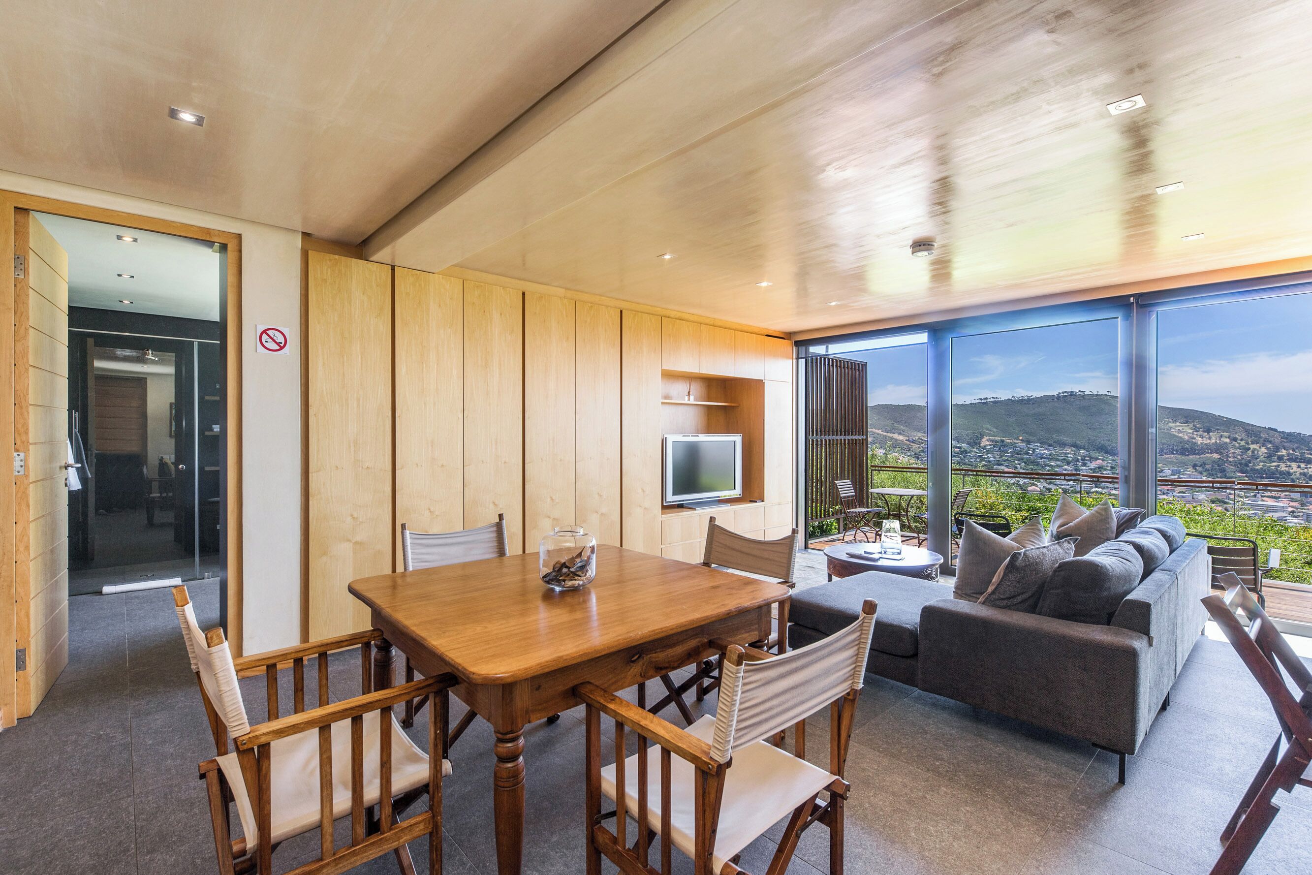 A modern interior with a wooden dining table, chairs, a sofa, and a TV.