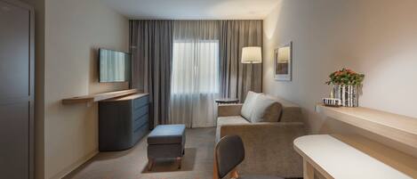 A hotel room with a flat-screen TV, a sofa, a desk, and a chair.
