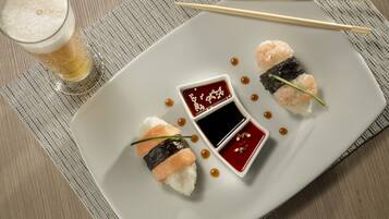 Un plato con sushi y dos recipientes pequeños de salsa, sobre un tapete texturizado.