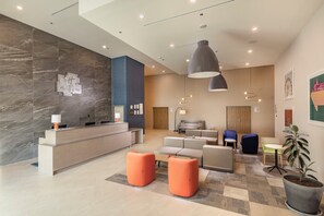 A hotel lobby with a reception desk, seating area, and a large plant.