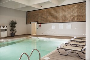 An indoor swimming pool with lounge chairs, a potted plant, and informational signs on the wall.