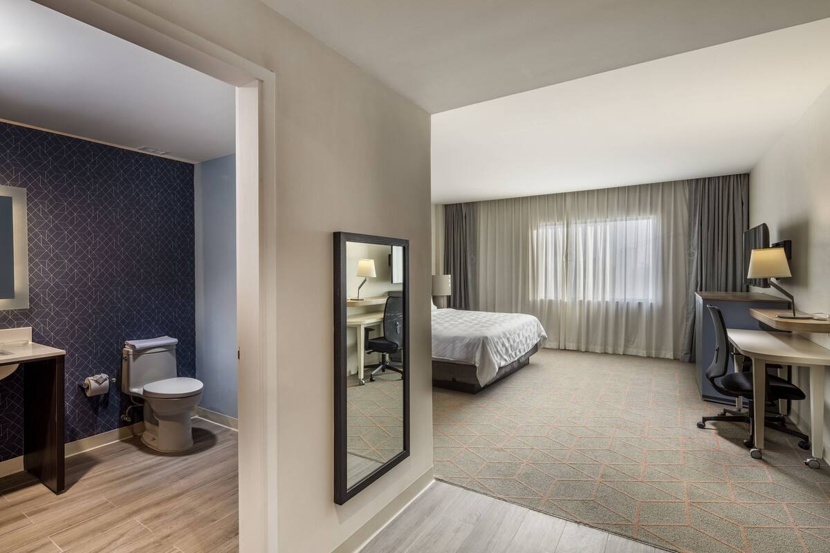 A hotel room with a bed, desk, chair, and a bathroom with a toilet and sink.