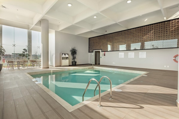 A modern indoor swimming pool with clear water, a tiled deck, and a view of the city through large windows. - Holiday Inn & Suites Aguascalientes by IHG (Aguascalientes)