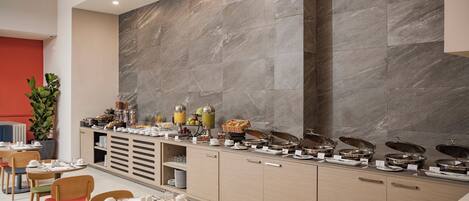 Un buffet de petit-déjeuner moderne, avec un mur arrière en marbre, des tables et des chaises disposées avec soin.