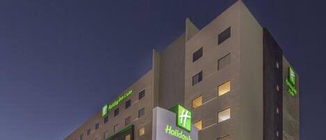 Un hotel Holiday Inn Express dal design moderno, con un evidente cartello verde e una facciata ben illuminata.