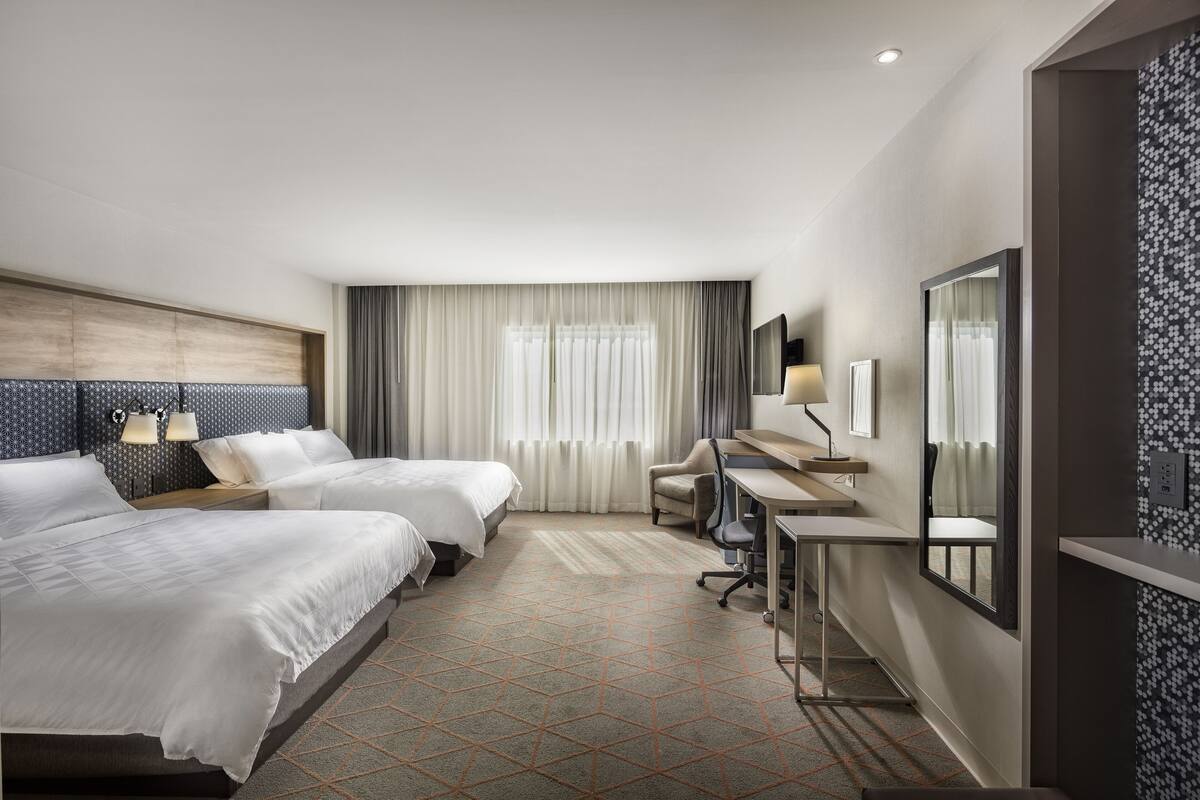 A hotel room with two beds, a desk, a chair, a TV, and a large mirror.