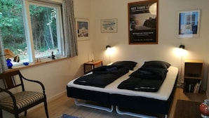 A bedroom with a bed, two bedside tables, a chair, a window with curtains, and artwork on the walls. - Penalhuzet (Ronne)