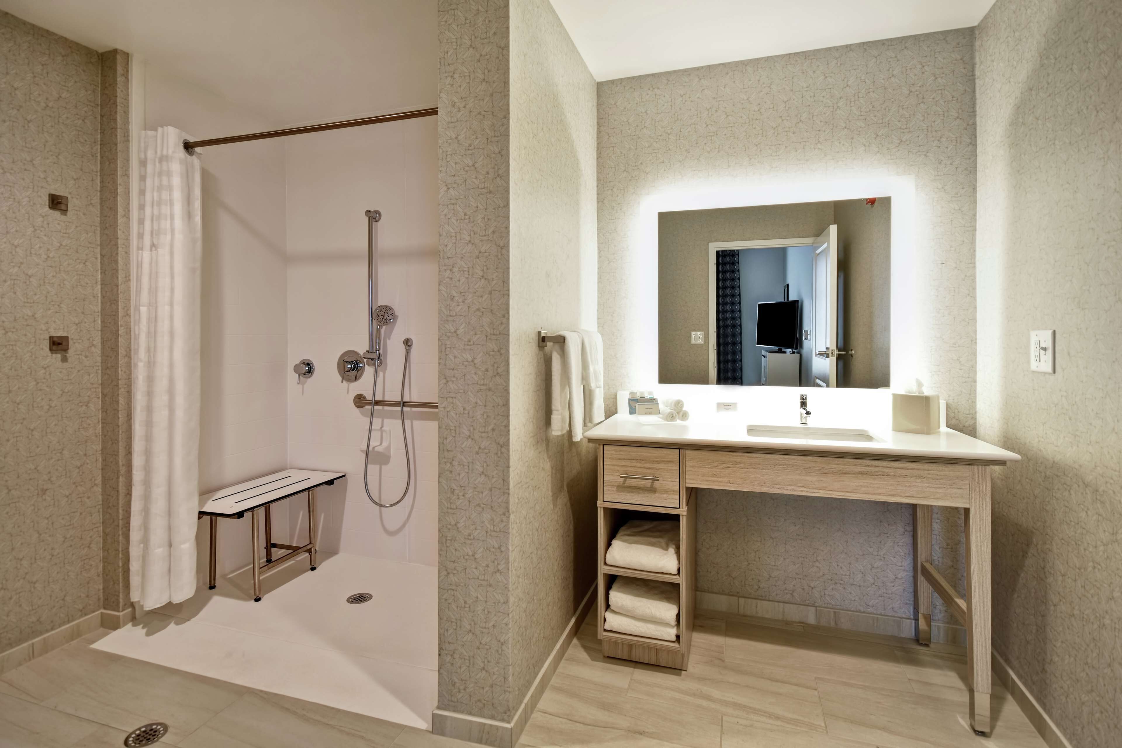 Ein modernes Badezimmer mit Dusche, Waschtisch inklusive Spiegel und einer Sitzbank.