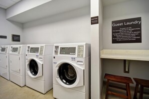 A laundry facility with multiple white front-loading machines, a sign indicating guest laundry use, and operating instructions. - Homewood Suites by Hilton Greenville Downtown (Greenville)