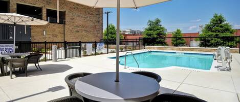 An outdoor pool area with a table and chairs, a brick building, and a sign indicating shallow water and no diving.
