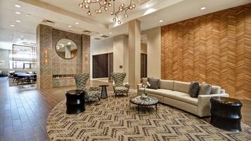 Um hall amplo com um lustre moderno, carpete estampado e uma área de estar com sofá e poltronas.