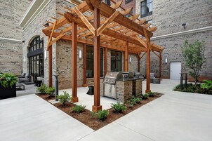 Un patio exterior con una pérgola de madera, una parrilla y una zona de estar.