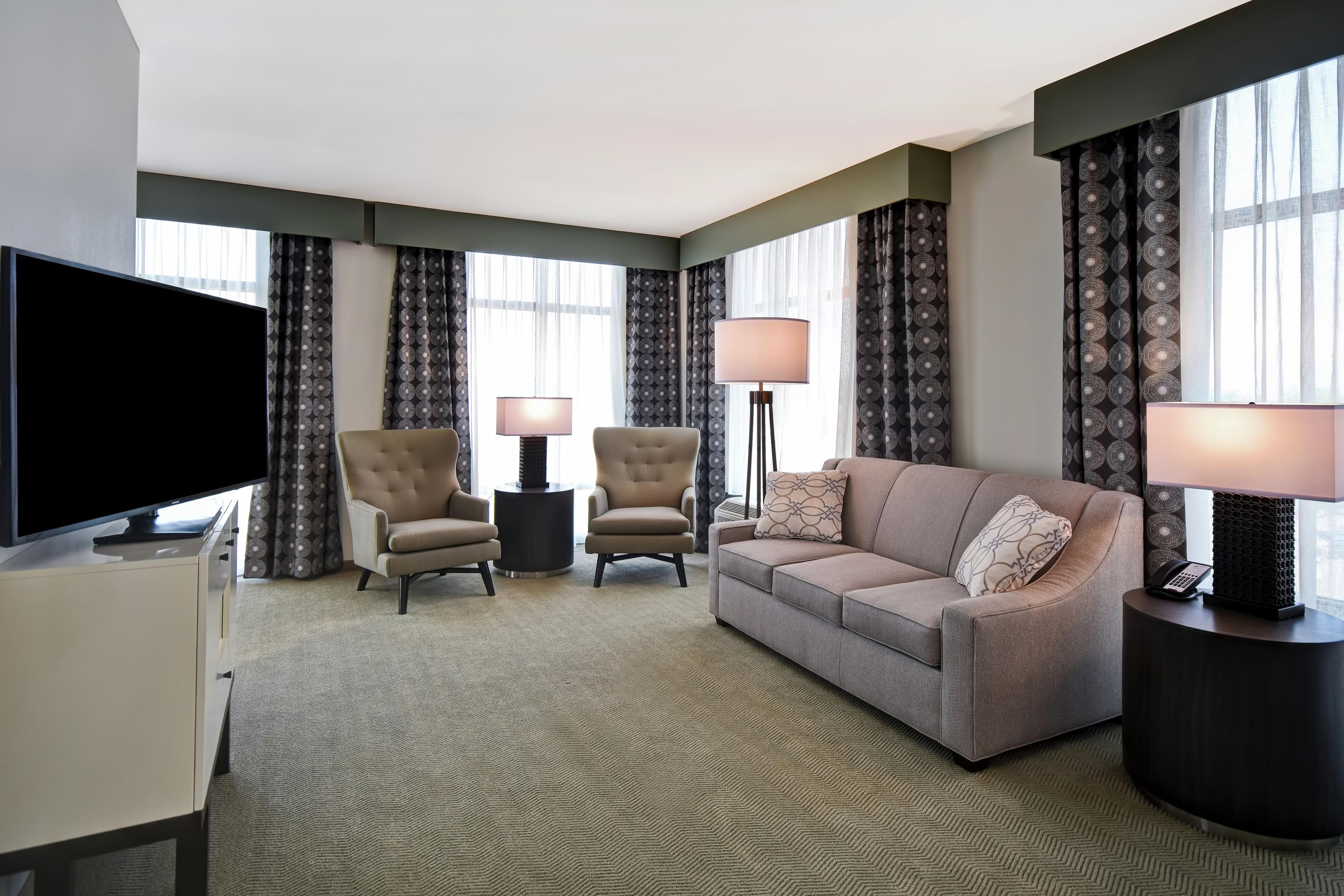 A hotel room with a flat-screen TV, two armchairs, a sofa, a coffee table, and a lamp.