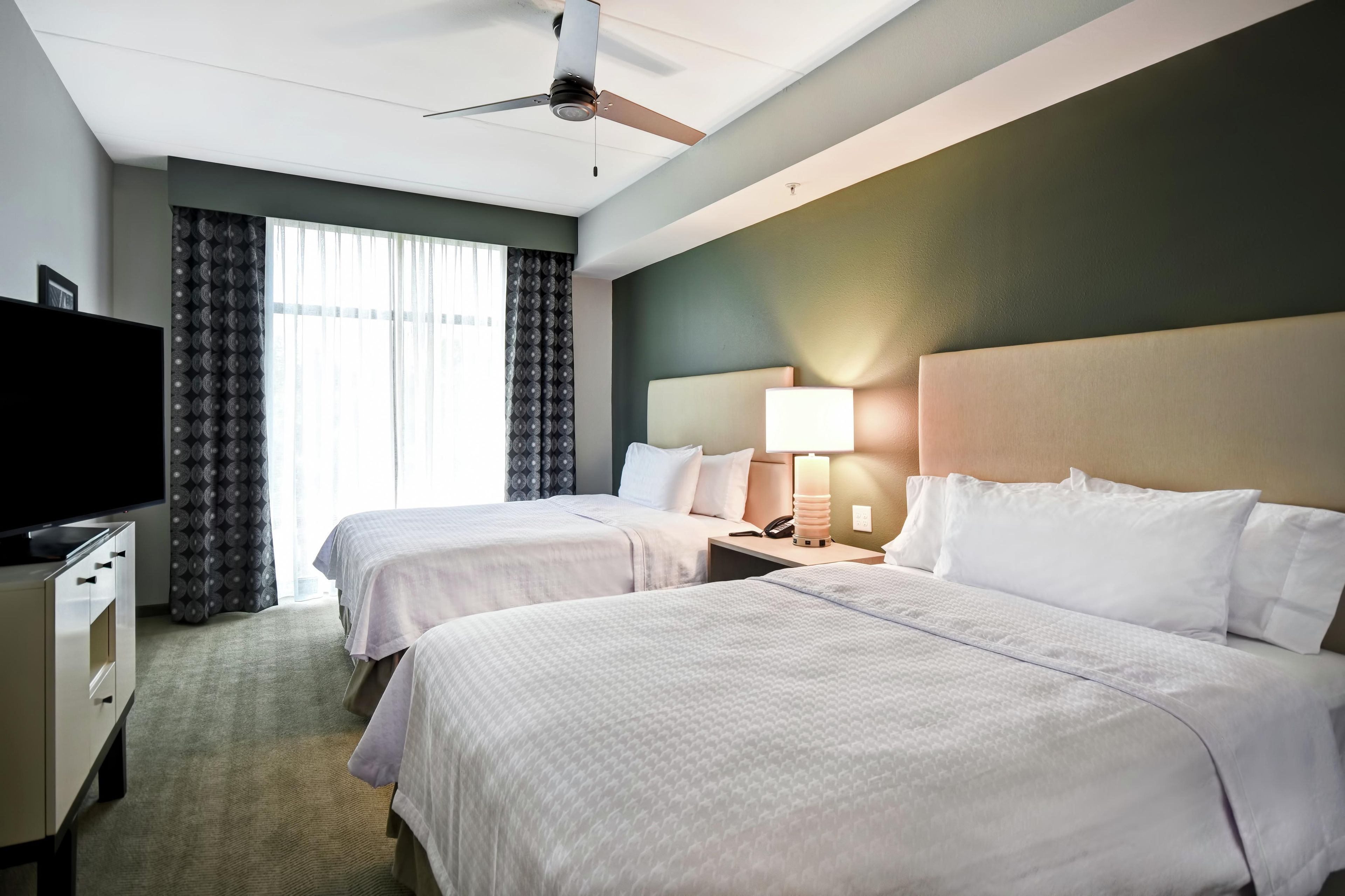 A hotel room with two beds, a TV, a desk, and a ceiling fan.