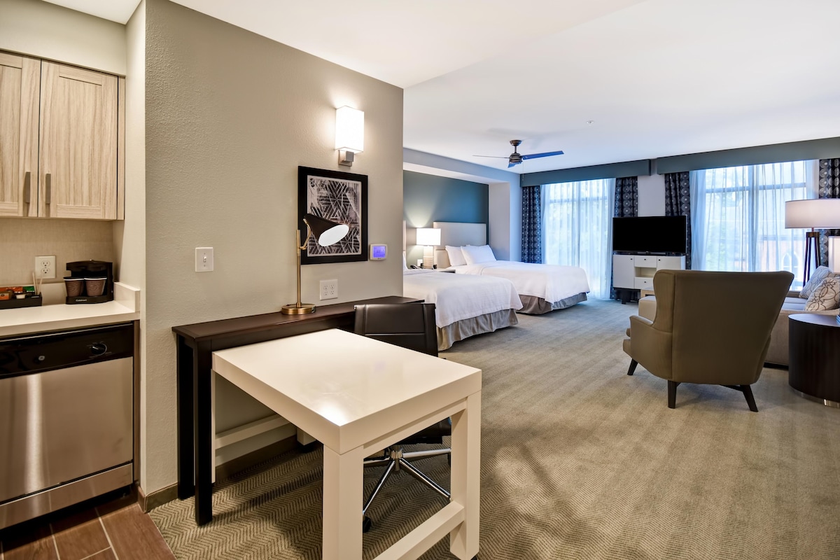 Een hotelkamer met een kitchenette, een bed, een bureau en een stoel.