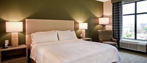 A hotel room with a large bed, two bedside tables with lamps, a chair, and a large window with a city view.