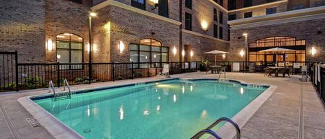 An indoor swimming pool with a brick wall backdrop, a poolside area with tables and chairs, and a clear pool edge.