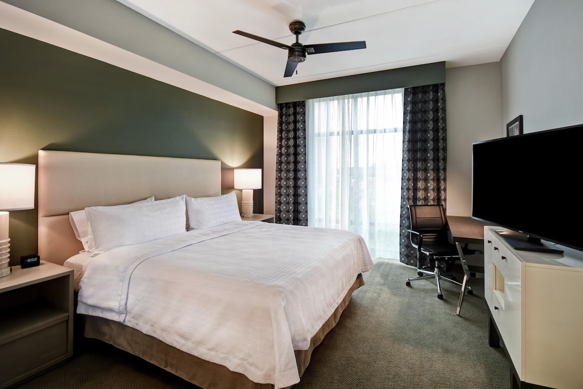 Een hotelkamer met een bed, een bureau, een televisie en een plafondventilator.