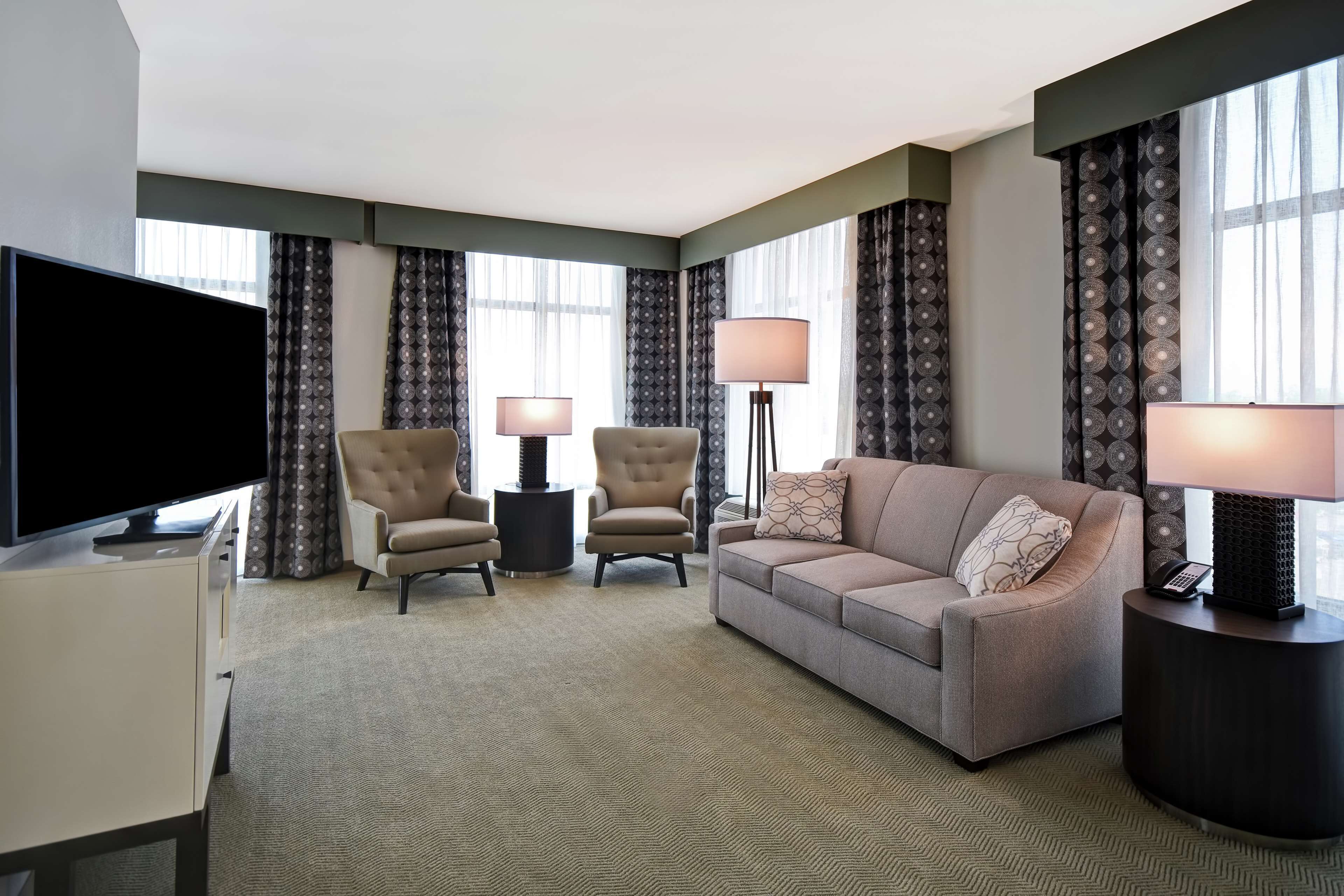 A hotel room with a flat-screen TV, two armchairs, a sofa, and a lamp on a side table.