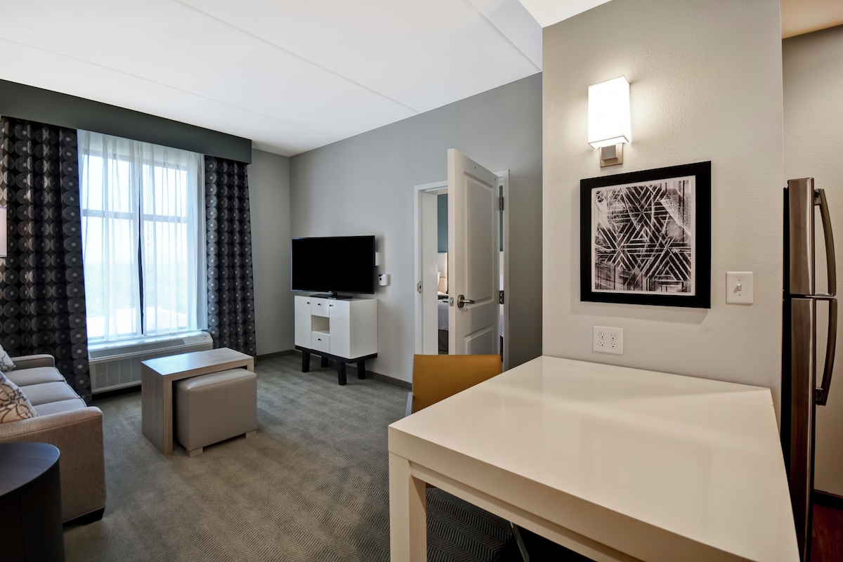Een hotelkamer met een flatscreen televisie, een eettafel, een bank en een wanddecoratie met een patroon.