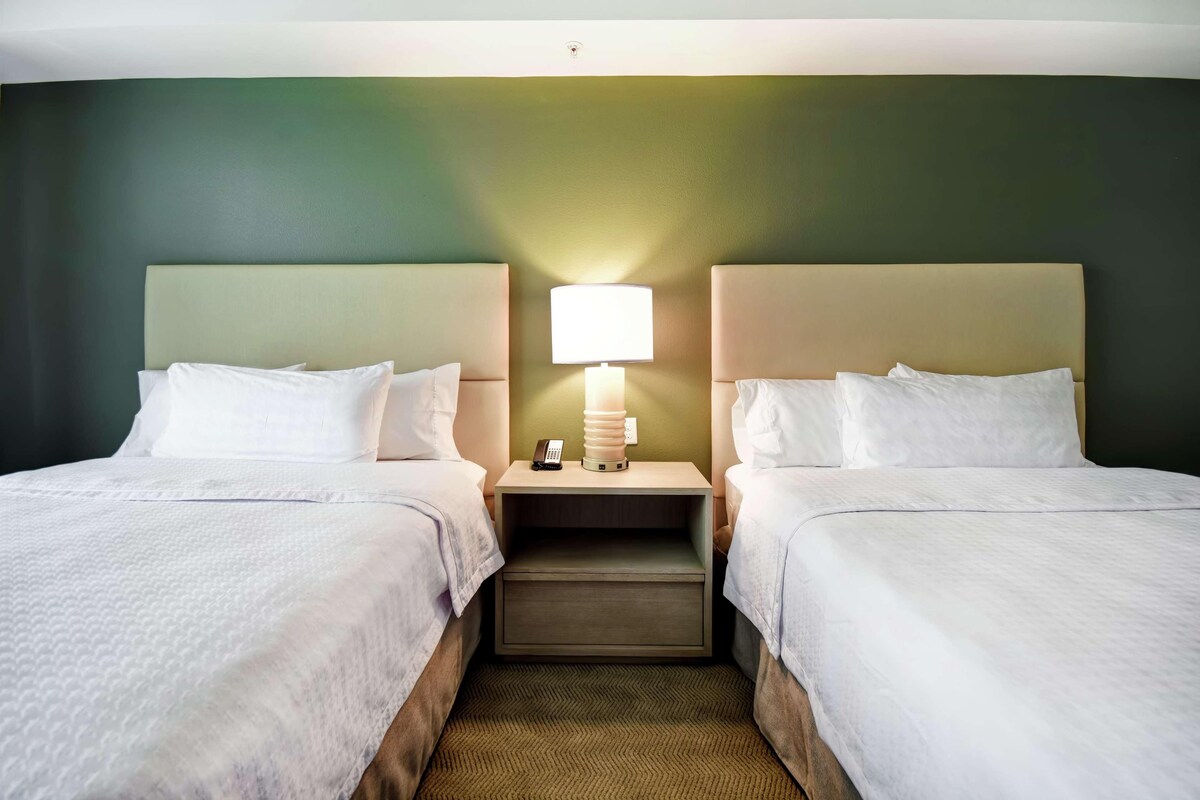 A hotel room with two beds, a nightstand with a lamp, and a small drawer.