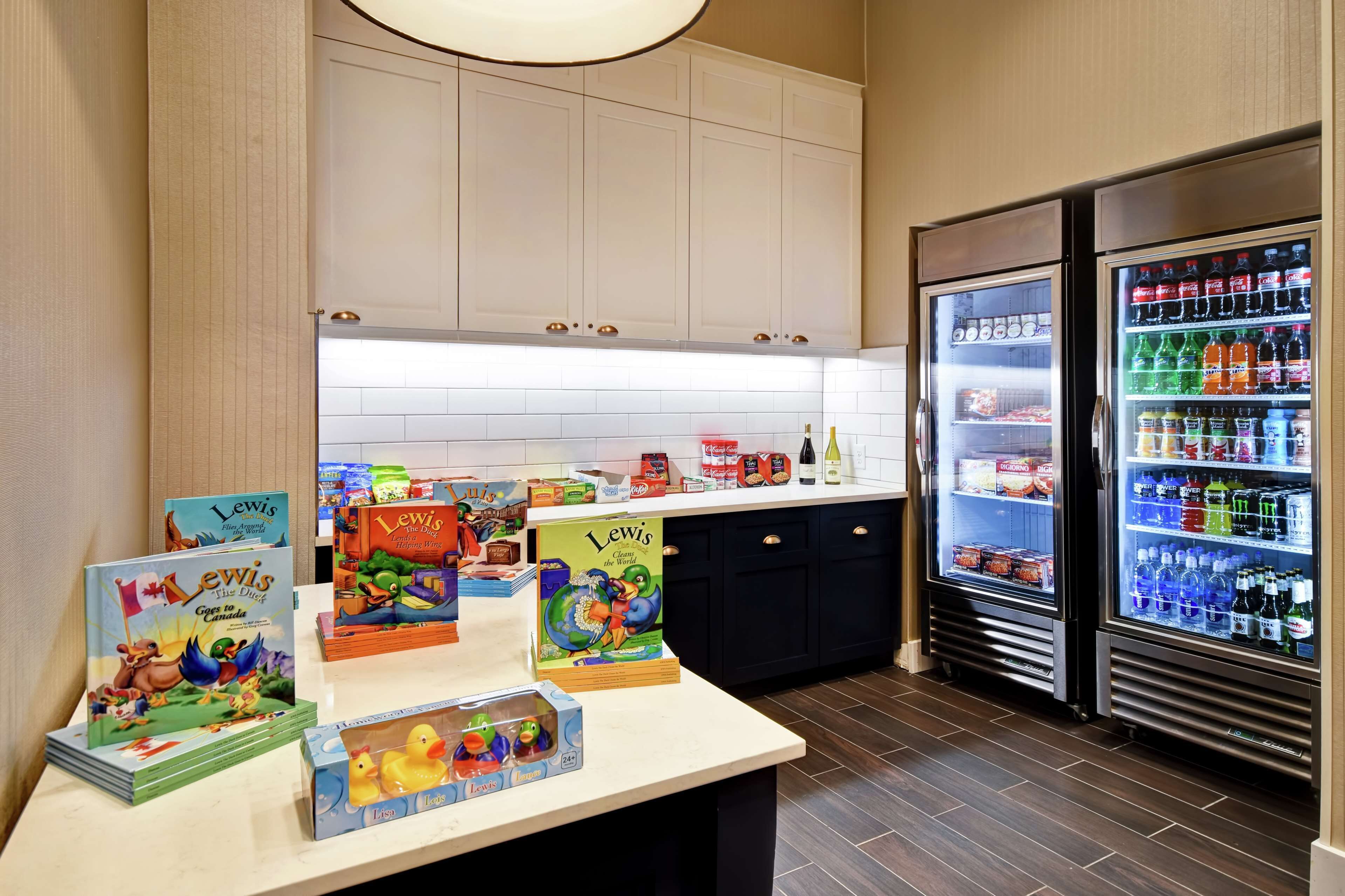 Una zona de cocina con mostrador que exhibe libros y juguetes infantiles, y dos refrigeradores llenos de bebidas.